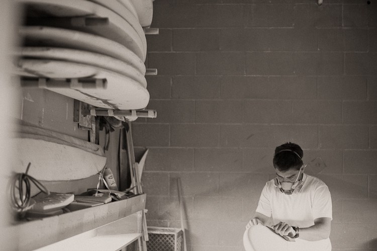 Breno refining a surfboard beneath the shaping-room board racks