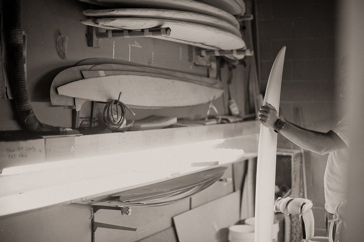 Breno inspecting a surfboard rail in the shaping bay